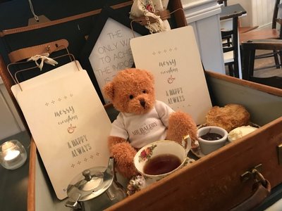 Photo of Mr Baldry (a teddy bear mascot) sat in a tray with tea, cakes and cards.