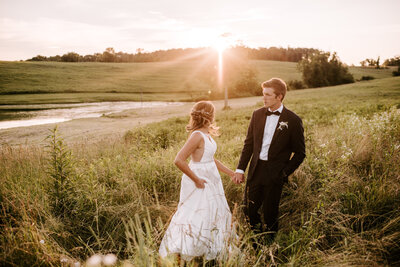 bride and groom holding hands while standing in field