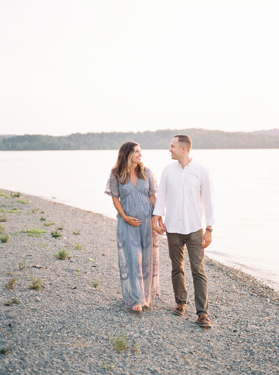 Couple walking together beside a lake at their maternity photo shoot