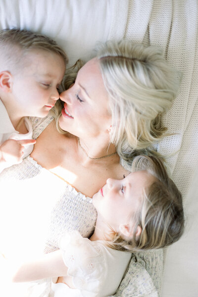 Image of mother and children's faces close to each other laying on bed taken by Sacramento Maternity Photographer Kelsey Krall
