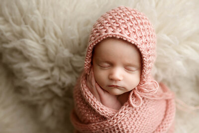 Baby girl swaddled in a pink knit blanket with matching bonnet.
