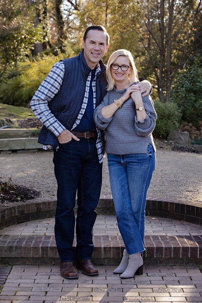 Elegant autumn portrait of parents standing together near brick terrace steps at UNCC Botanical Garden Charlotte NC, smiling confidently at the camera