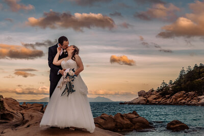 newly wed husband and wife sharing a sunset kiss on the beach in Townsville - Wedding Photography by Simmomns Memorable Moments