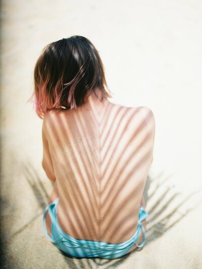 Shadows on the spine of a girl with pink tipped hair on the beach in a blue swimsuit for her boudoir session in Puerto Rico.