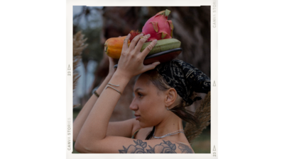 Jewelry model woman of color with tattoos poses for small business jewelry line with a plate of fruit on her head