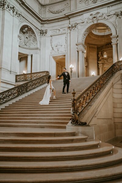 bride and groom walk up the grand stair case of san francisco city hall