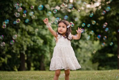 little girl in white floral dress looking and playing with bubbles
