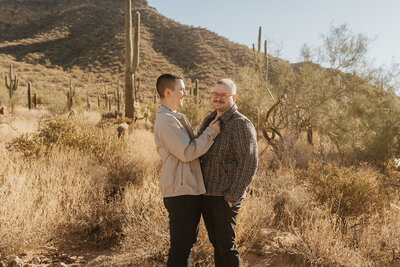 A couple standing in the desert smiling with their arms on one another 