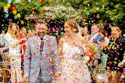 a bride and groom exiting their outdoor ceremony to colourful confetti