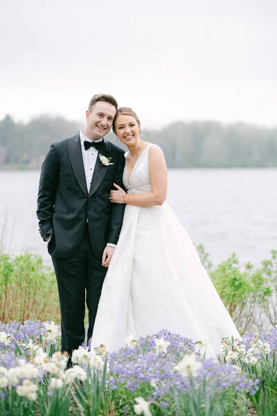 Bride and Groom snuggle up in a bed of flowers in front of a lake