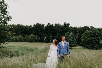 bride and groom holding hands while standing in field