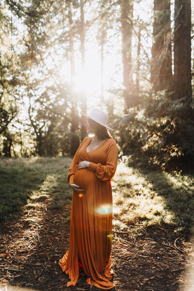 Mom holds her pregnant belly as the sunlight hits her