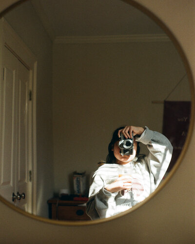 woman holding waist level camera in front of mirror
