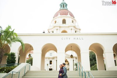 Groom to be holds his Bride from behind and whispers in her ear on the steps of Pasadena City Hall