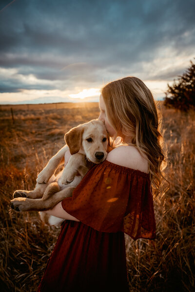 woman snuggles golden retriever dog at sunset