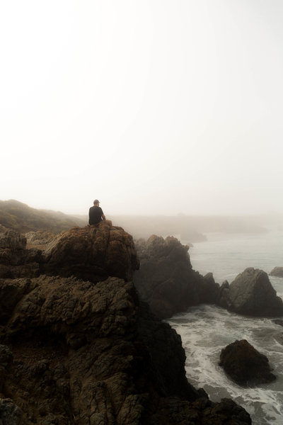 ATlanta Wedding Photographer Grant Bingham sit on cliff looks at ocean