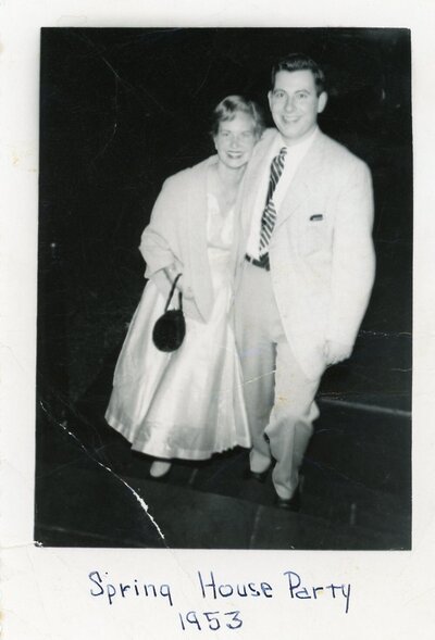 Vintage polaroid of couple dressed up, hugging and smiling at camera. Writing in blue pen reads 'Spring House Party 1953'