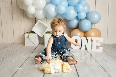 1 Year old dressed in overalls enjoying a delicious cake.