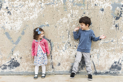 2 young kids standing in front of a wall