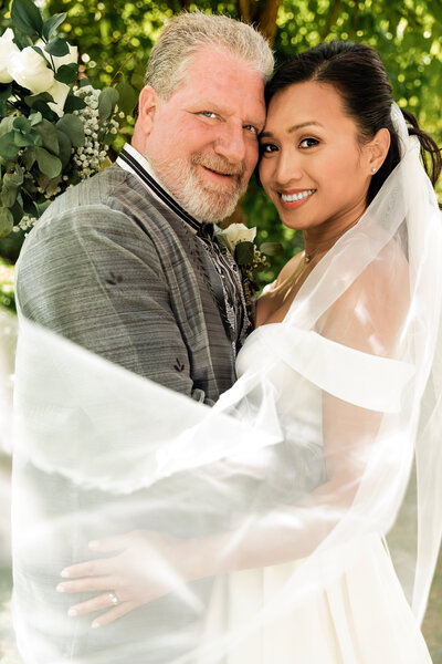 veil blows over brides shoulder as bride and groom embrace