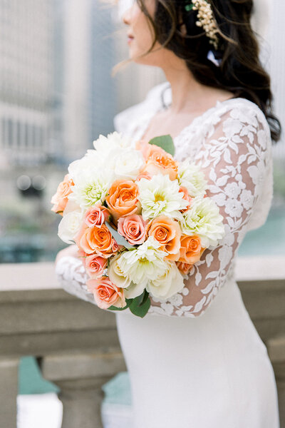 image of bride holding coral bouquet in front of chicago's riverwalk skyline