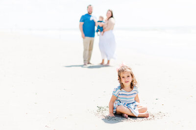 Daughter sits in front of rest of family during family photo session with Ron Schroll Photography at Ocean Isle Beach, NC