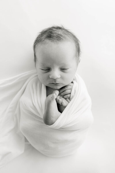 black and white image of newborn baby swaddled with his hands and feet close to his chin