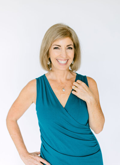 Lora Ulrich, menopause Health Coach in a teal top smiling warmly at the camera.