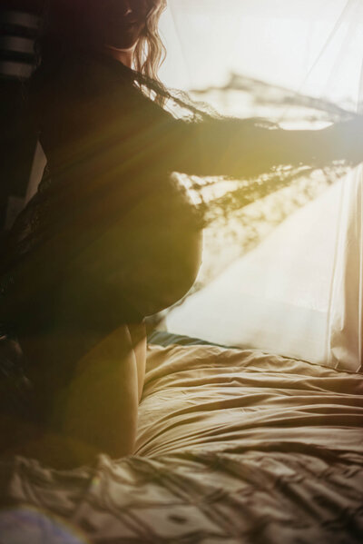 Maternity Photographer, pregnant woman kneeling on bed with sunlight shining behind her