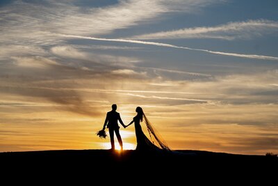 Bride and groom holding hands against a sunset