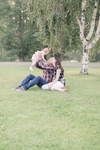 PNW Elopement Photographer captures father lifting baby while sitting in grass