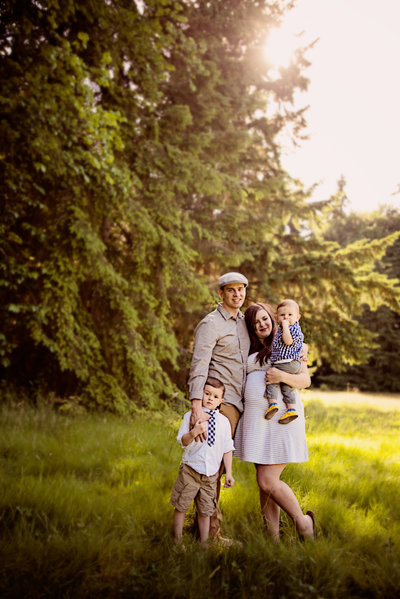 Colorful image of two young boys and their pregnant mother in a white dress and dad in a hat