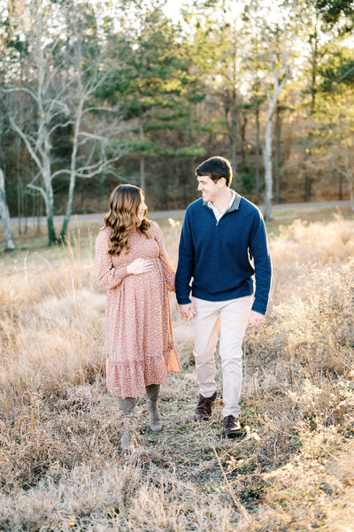 Expecting couple holding hands walk together during maternity photo session outdoors in Raleigh NC