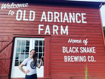 Woman holding a beer in front of a red barn