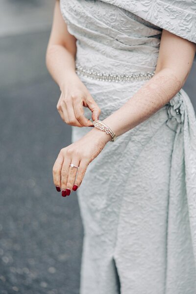 A woman in an elegant grey dress with bead detailing adjusts her bracelet.