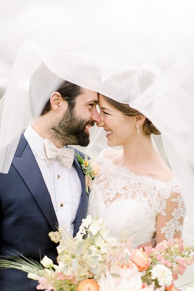 bride and groom laughing together under veil