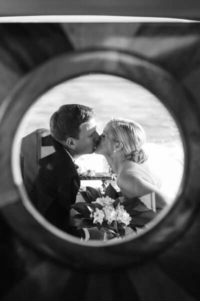 Black and white newlyweds kissing on boat through round window