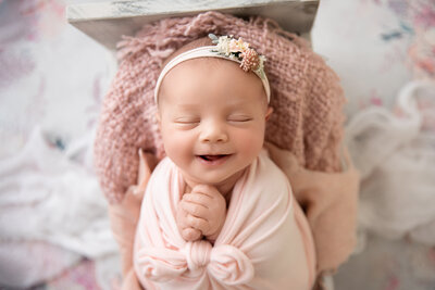 newborn baby girl posed on a pink lace blanket in a sleeping position wearing a pink headband