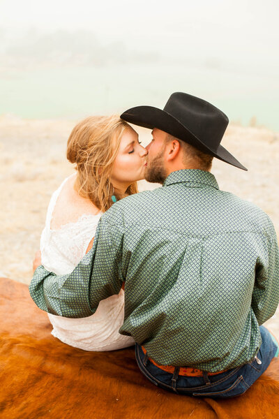 A woman in a wedding dress, kissing her husband in a cowboy hat.