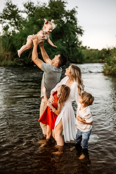 Family Photographer,  Family stands in a river with a dad tossing baby in air