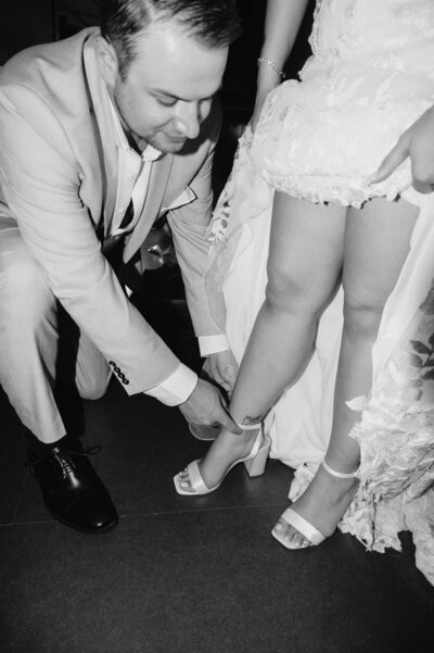Black and white flash photography wedding day photojournalism style groom tying bride's wedding day shoes
