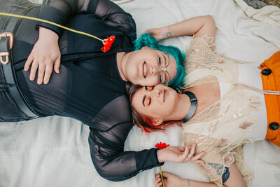 Two ladies with colorful hair laying side by side with their eyes closed