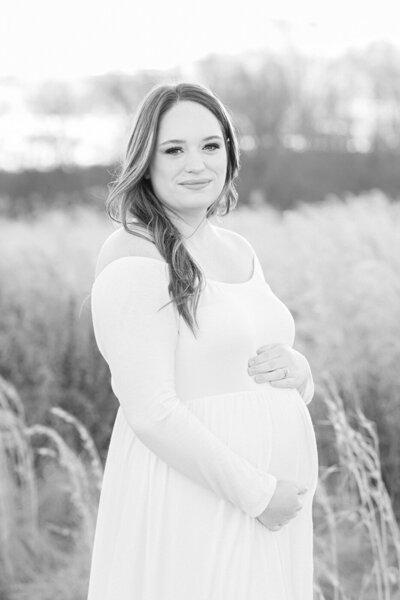 pregnant woman in field in white dress holding belly maternity pictures