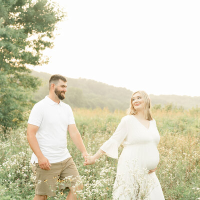 Pregnant couple walk through field of flowers at Louisville Ky park during outdoor photo shoot with Julie Brock Photography