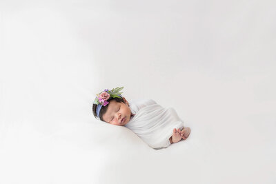 Posed newborn baby wrapped in a white swaddle