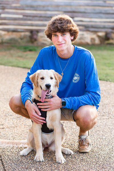 High school senior boy with his dog sitting at a park in Wake Forest.
