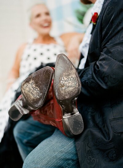 Bride wearing red cowboy boots props her feet up on the groom's lap