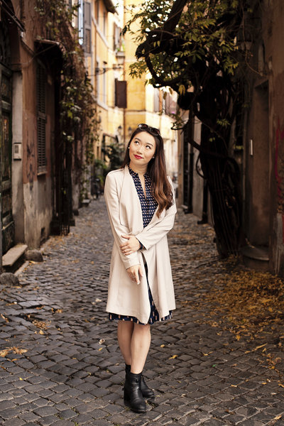 A girl in a cream coat standing on a cobblestoned street looking up. Taken by Rome Solo Travel Photographer, Tricia Anne Photography
