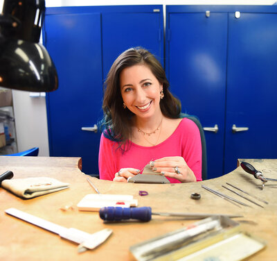 jewelry maker sitting at her workstation with blue lockers behind her