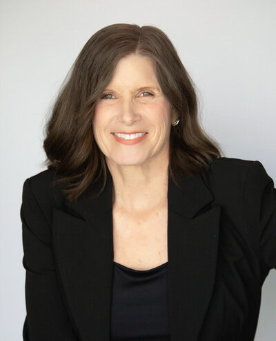 Headshot of Deborah Lytton, a woman with brown hair and hazel eyes wearing a black suit jacket over a black top